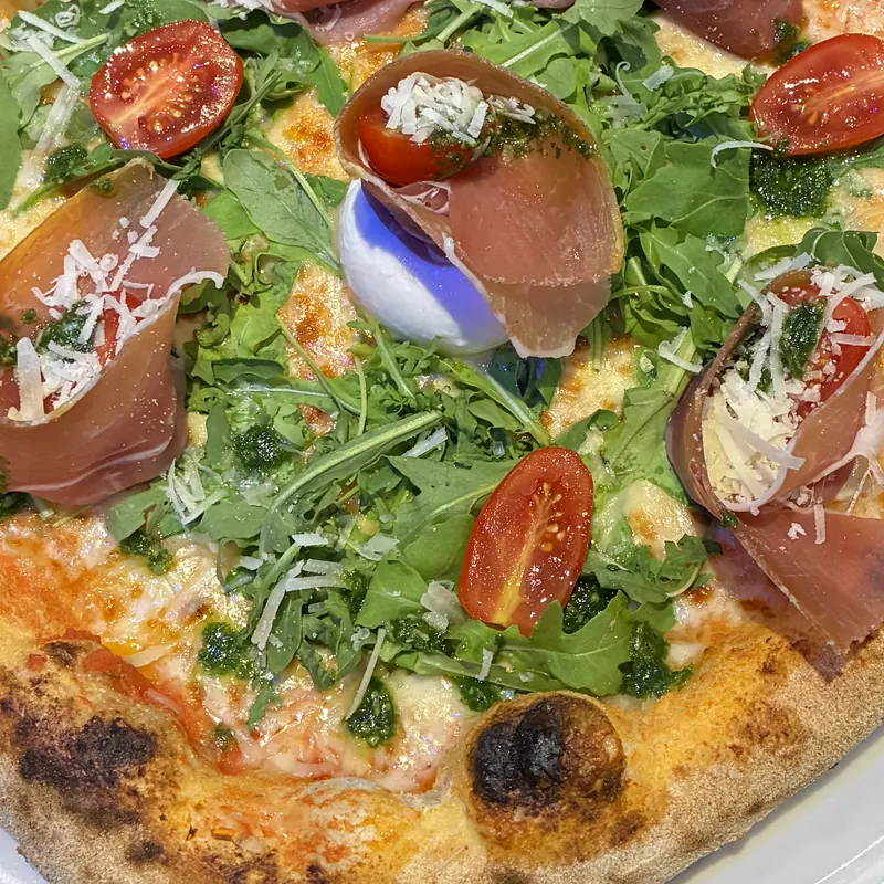 Nahaufnahme einer neapolitanischen Pizza mit Rucola, Parmaschinken, Cherrytomaten, Burrata und Pesto