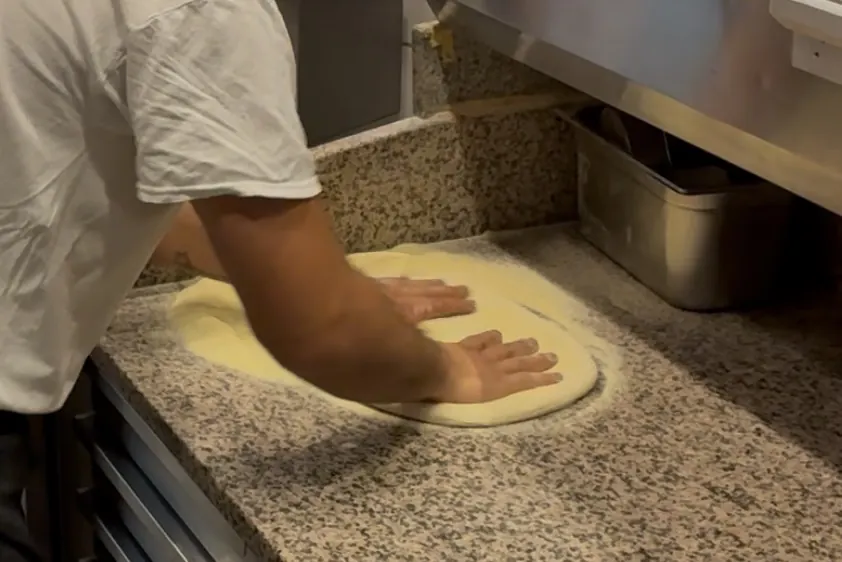 Der Pizzaiolo treibt den Teig mit den Handflächen auf der Steinplatte nach außen