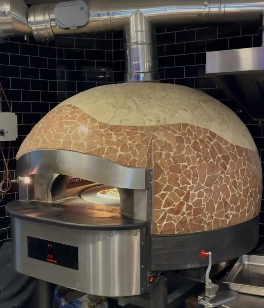 Der neapolitanische Steinofen mit Mosaikkuppel, im glühenden Ofenmaul backt eine Pizza; die Anzeige steht auf 377 Grad