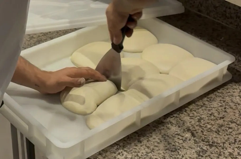 Gereifte Teigballen in der Gärbox, der Pizzaiolo löst einen mit dem Teigheber heraus