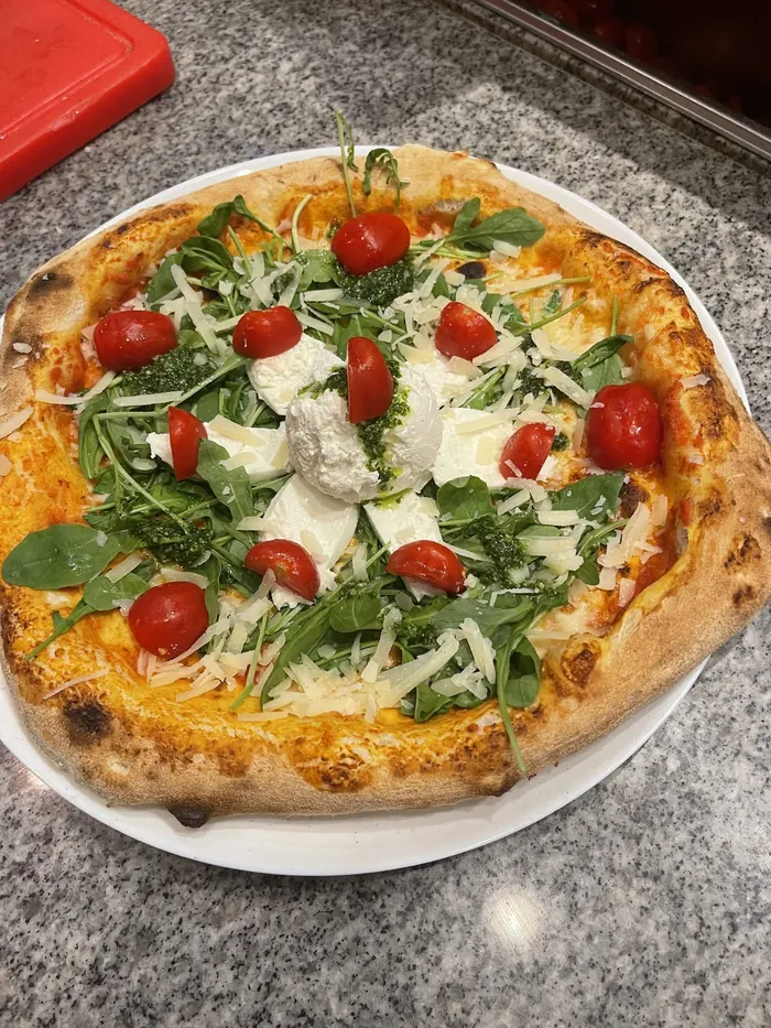 Pizza mit Mozzarella, Rucola, Cherrytomaten, Parmesan und Pesto, frisch aus dem Steinofen